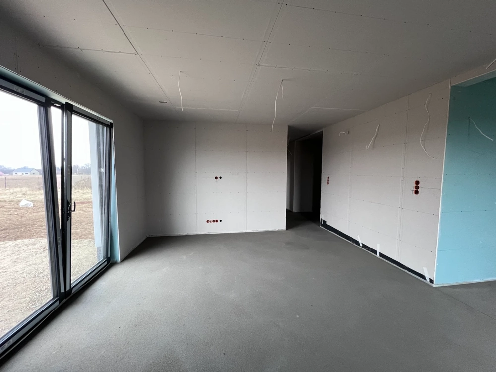 Przestronne wnętrze domu w stanie deweloperskim z betonową wylewką, ścianami z płyt g-k, zawieszonymi przewodami i dużymi przeszkleniami